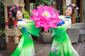 two beautiful asian girls in traditional chinese blue and green dresses with umbrella in a form of lotus flowers