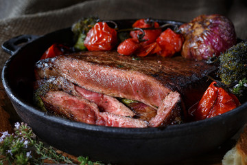 Beef steak medium rare pieces with a garnish of vegetables in a cast iron skillet. meat shot in low key. fatty foods rich in protein.