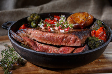 Beef steak medium rare with vegetables on a cast iron skillet. Still life of meat and vegetables in a low key. Rustic style food. covered with a rustic table