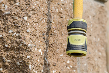 Yellow garden hose with the fixing coupling with the inscription "STOP" against the stone block