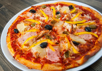 Hawaiian pizza with pineapple, ham, chicken, cheese, olives and vegetables on a wooden table