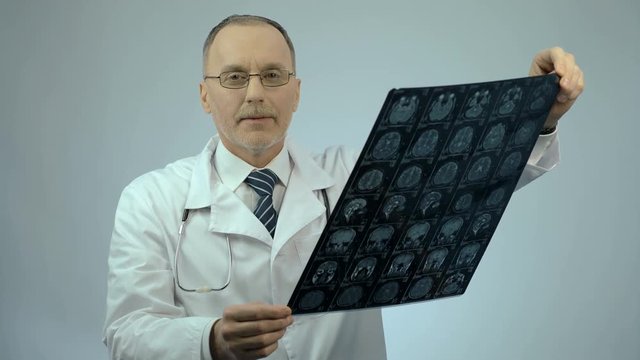 Neurosurgeon checking MRI brain image, looking at camera, health care services
