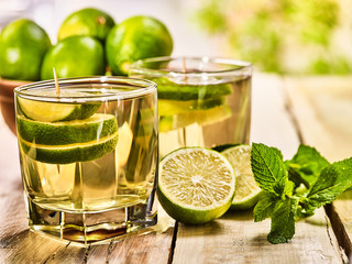 Country drink. On wooden boards are two glasses with green transparent drink and lime glue bowl. A drink number nineteen mojito with mint leaf on sunlight . Country life. Light background.