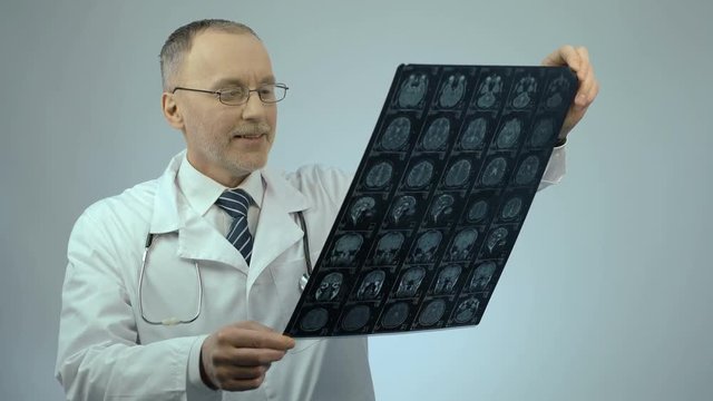 Happy smiling doctor checking MRI brain scan, satisfied with treatment results