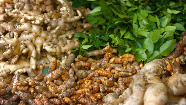 Video 3840x2160 - Slow, shifting, selective focus shot of a vendor's stall at an Asian public market, selling ginger, turmeric and Kafir lime leaves.