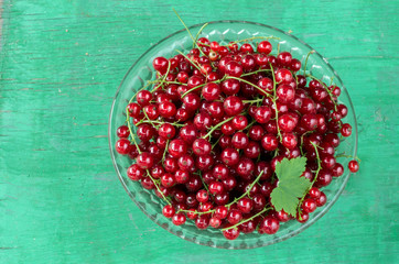 Red currants in a clear glass bowl on a background of painted wood.