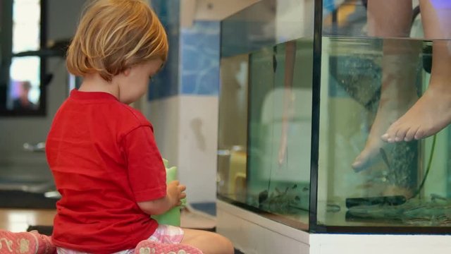 Cute baby playing in the fish-spa beauty saloon.