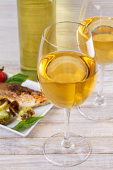 Glasses and bottle of white wine. Grilled dorado fish with vegetables in white plate