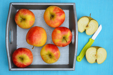 close up of red, yellow ,green apples in a wooden tray bowl with red white nostalgic  countryside checkered doily
