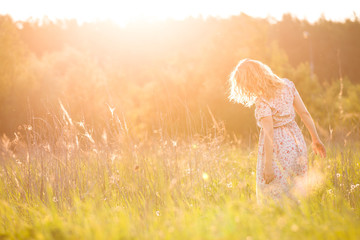 Portrait of happy young blond woman running on a meadow on a sunny summer day. Girl dancing on the...