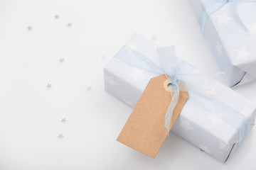 Top view on nicely wrapped gifts in the paper with stars and light blue ribbon  and mock-up tag on the white background. Presents for birthday, Christmas or any celebration. Holidays concept.