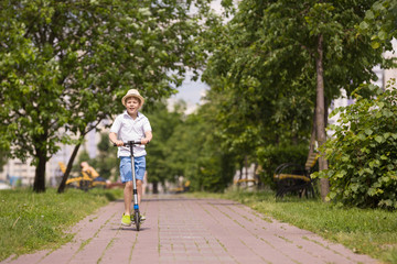 Fototapeta premium Cute kid boy riding his scooter and having fun in the park on a sunny day. Activities with children outdoors. Child on scooter. Lifestyle and active leisure concept.