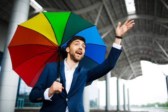 Picture of  young businessman holding motley umbrella waving hand