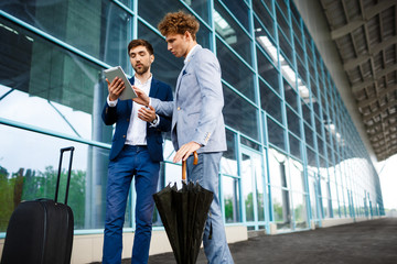 Picture of  two young businessmen talking on airport background and holding tablet