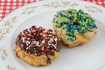 Two frosted donuts, vanilla and chocolate, with sprinkles on white plate