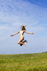 Obraz premium The happy woman in white bikini jumps in a summer green field against the blue sky.