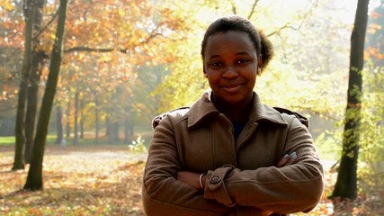 Young beautiful happy african girl stare into camera cross one´s arms and stands in the woods - eye contact 