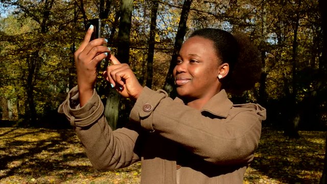 Young beautiful african girl stands in woods, observes landscape and makes a photos