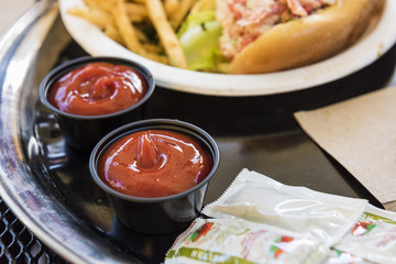 Ketchup in cups with relish packets and fast food on a mesh table