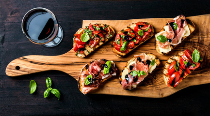 Brushetta set and glass of red wine. Small sandwiches with prosciutto, tomatoes, parmesan cheese, fresh basil, balsamic creme on rustic wooden board - obrazy, fototapety, plakaty