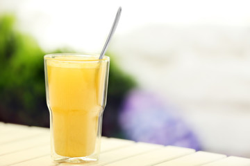 Full glass of juice with spoon on light wooden table