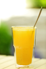 Full glass of juice with spoon on light wooden table