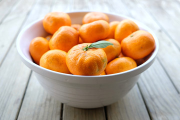 Imperfect satsuma mandarins - organic fruit produce - in a white bowl on a wooden background. Photographed with shallow depth of field in New Zealand. - obrazy, fototapety, plakaty