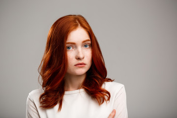 Portrait of young beautiful ginger girl over gray background.