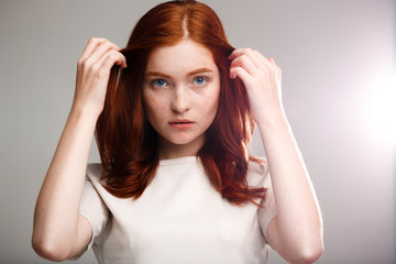 Portrait of young beautiful ginger girl over gray background with back light.