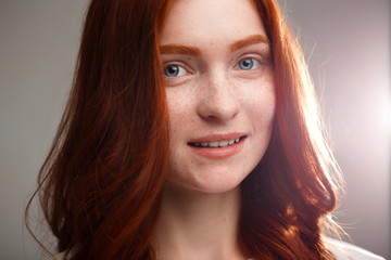 Portrait of young beautiful ginger girl over gray background with back light.