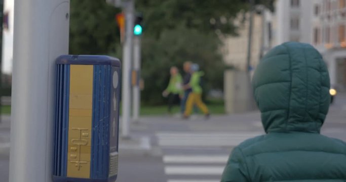 Child pushing the button on traffic lights and then he with mom crossing the road on green signal