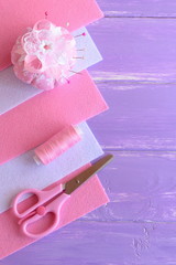 Pink and white felt sheets, pincushion, thread, needles, pins, scissors on lilac wooden background with copy space for text. DIY hand sewing set. Needlework background