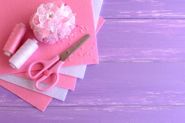 Pink and white felt sheets, needle cases, thread, needles, pins, beads, scissors on lilac wooden background with copy space for text. Needlework kit