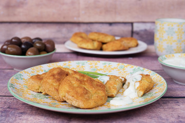 Baked potato meatballs balls in a yellow plate. Back olives and yogurt sauce. Closeup, fresh tones. wood background