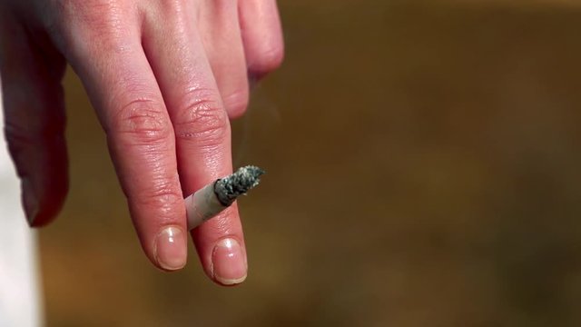 Slowmotion detail of woman´s finger which holds a cigarette 