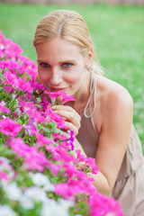 Fototapeta premium Beautiful blonde young woman smells flowers in a garden
