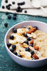 Bowl of homemade oatmeal porridge with banana, blueberries, almonds, coconut and caramel sauce on teal rustic table, hot and diet food for Breakfast
