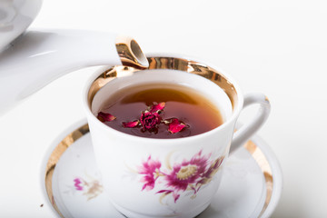 Old-style porcelain kettle pouring tea from jug to cup of tea