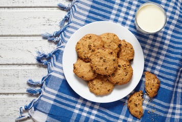 Homemade traditional oatmeal cookies with raisins healthy sweet dessert snack food with glass of milk and blue napkin on white vintage wooden table background