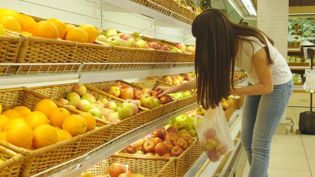Woman selecting fresh red apples in grocery store produce department and putting it in plastic bag. Young pretty girl is choosing apples in supermarket and putting them into shop basket