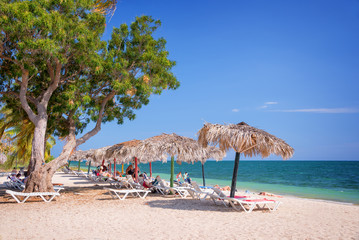 Tourists relaxings on beach chairs and straw umbrellas on Ancon beach, Trinidad, Cuba