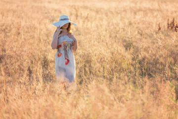 Portrait of a young woman, wearing a white hat, in a wheat field, at sunset
