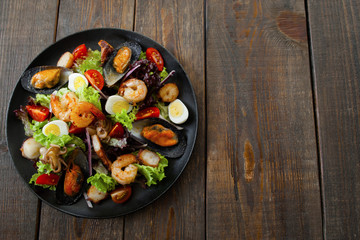 Fototapeta na wymiar Grilled seafood salad on wood flat lay copyspace. Top view on black plate with salad with grilled seafood and quail eggs, free space