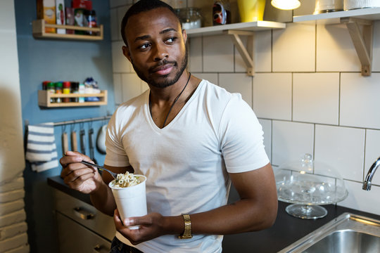 Handsome young black man eating take out food at home.