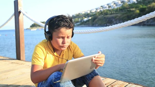 Boy playing digital tablet  computer on wooden pier by the sea