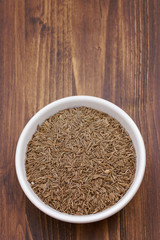 carum in white bowl on brown wooden background