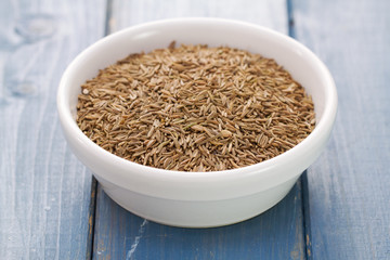 seeds of carum in white bowl on blue wooden background