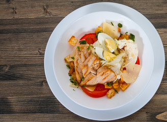 Caesar salad with croutons, cheese, eggs, tomatoes and grilled chicken on wooden table