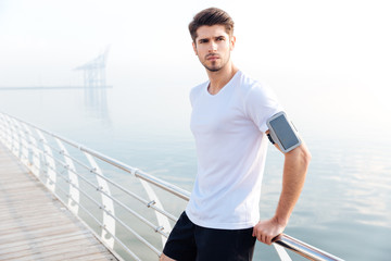 Fototapeta na wymiar Confident sportsman with cell phone on armband standing at pier
