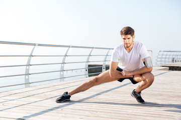 Young sportsman stretching legs during workout on pier